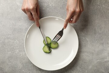Bulimia. Woman cutting cucumber at grey table, top view