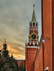 Majestic clock tower rises against a vibrant sunset sky near red brick walls adorned with winter...