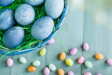 Naturally dyed blue Easter eggs in a basket with candy in background. Selective focus with blurred background.