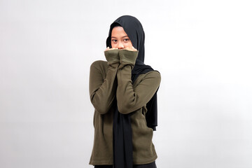 Indonesian woman in a black hijab and olive green sweater, posing shyly with hands covering her...