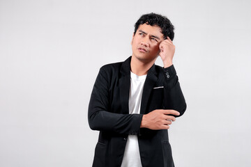 Asian man in black blazer and white t-shirt touching temple, looking up with a thoughtful expression. Isolated on white background.