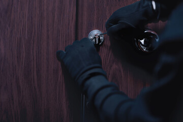 Closeup of unrecognizable robber cracking door lock with metal picklock tool during house breaking