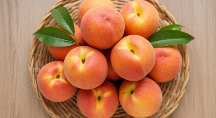 Fresh ripe peaches arranged on a wooden plate with green leaves, top-down view.