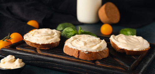 Wooden board of tasty sandwiches with cream cheese on black background