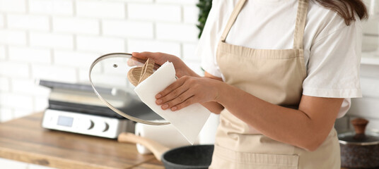 Beautiful young happy woman wiping dishware with paper towels in kitchen, closeup