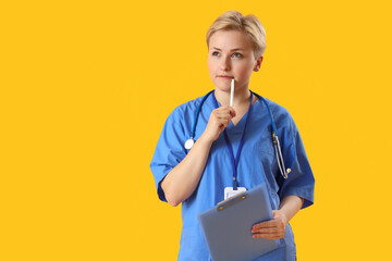 Thoughtful female medical intern with clipboard on yellow background