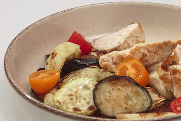 The image shows a bowl filled with a variety of grilled and roasted vegetables, along with sliced pieces of chicken. 