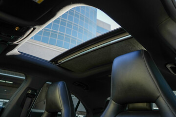 A car interior with a sunroof and two seats. The sunroof is open and the seats are leather