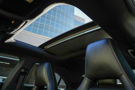 A car interior with a sunroof and two seats. The sunroof is open and the seats are leather
