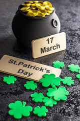 St. Patrick's Day. Green clover leaves decoration and cauldron with golden coins on black table.