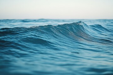 A single wave crests on a deep blue ocean under a pale sky.