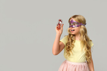 Funny little girl with noisemaker wearing carnival mask on light background