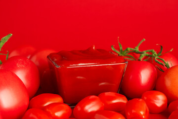 Ketchup in bowl and tomatoes on red background, closeup