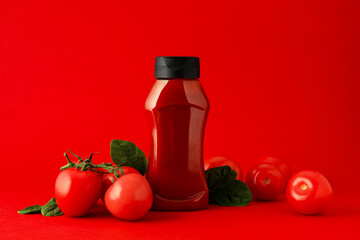 Bottle of ketchup and tomatoes on red background