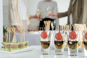 Many different tasty canapes on white table. People clinking glasses of wine indoors, closeup