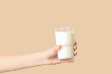 Selbstklebende Fototapeten Hand with glass of milk on beige background © Pixel-Shot