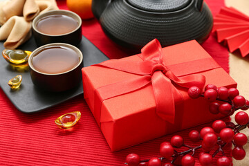 Gift box with cups of tea, berries and fortune cookies on red background. New Year celebration