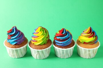 Delicious cupcakes with colorful cream on green background, closeup