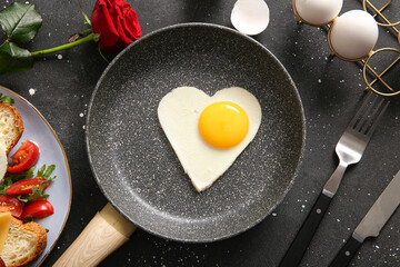 Frying pan with tasty fried egg in shape of heart and rose flower on dark background