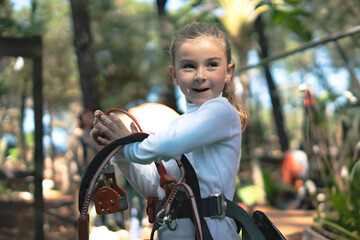 Girl wearing safety harness getting ready for zip line adventure in forest park