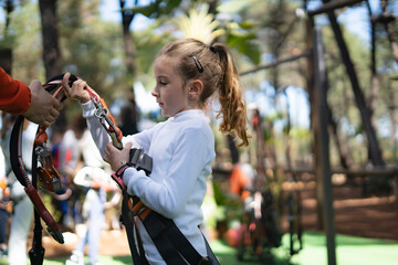 Instructor helping young girl putting on safety harness in adventure park