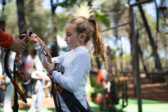 Instructor helping young girl putting on safety harness in adventure park