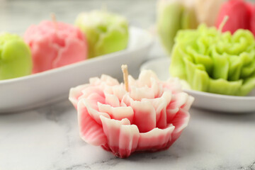 Beautiful flower shaped candles on white marble background, closeup