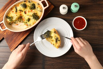 Woman eating tasty vegetable casserole at wooden table, top view