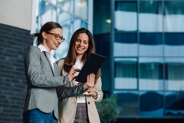 Two businesswomen using digital tablet outside office building