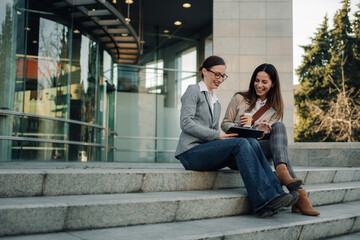 Two businesswomen using digital tablet and drinking coffee outdoors