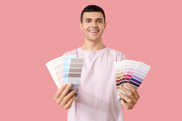 Young man with paint palettes on pink background