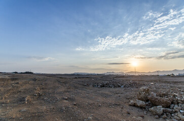Expansive desert scene under morning light. Soft sunlight casts gentle shadows over arid terrain. Cloud-dappled sky complements sandy hues in background