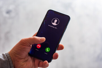 Close-up of a hand holding a smartphone with an incoming call screen. Display shows Incoming call...