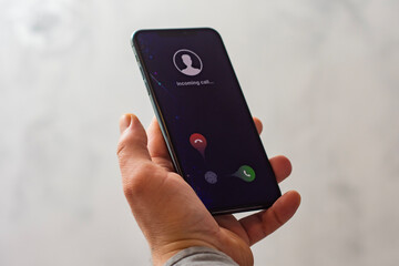 Close-up of a hand holding a smartphone with an incoming call screen. Display shows Incoming call with green accept and red decline buttons.