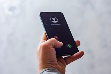 Close-up of a hand holding a smartphone with an incoming call screen. Display shows Incoming call...