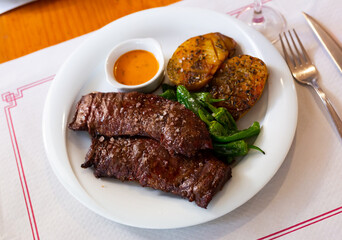 Appetizing roasted beef steak in chimichurri sauce served with baked potatoes. Spanish cuisine
