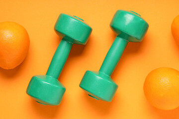 Pair of green dumbbells and ripe oranges on color background