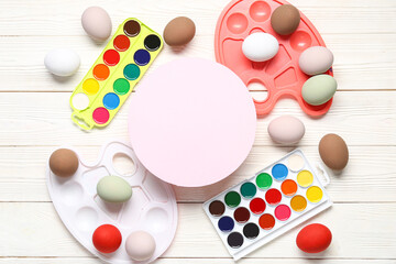 Frame made of Easter eggs, watercolors and blank card on white wooden background