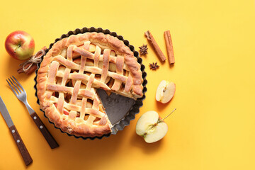 Tasty homemade apple pie with fruits, cinnamon and cutlery on yellow background