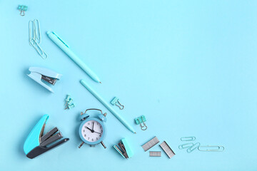 Blue staplers with staples, clips, pens and alarm clock on color background