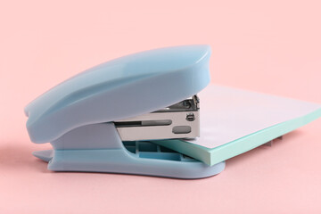 Blue stapler with sticky notes on pink background