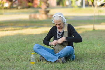 Middle-aged lesbian woman sitting on the grass in the park while listening to music with headphones and looking at her cell phone