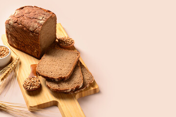 Wooden board with sliced loaf of bread, wheat spikelets and grains on grey background
