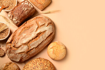 Loaves of fresh bread with buns and wheat spikelets on beige background