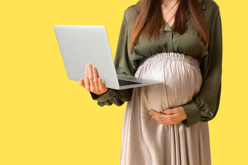 Young pregnant businesswoman with laptop on yellow background, closeup