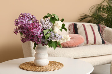 Vase with lilacs branches on coffee table in stylish living room