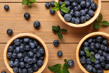 Bowls with sweet fresh blueberries and leaves on wooden background