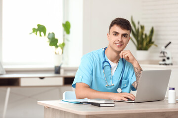 Fototapeta premium Young male doctor working with laptop at table in clinic
