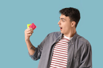 Shocked young man with condoms on blue background