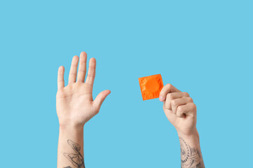 Male hands holding condom and showing stop gesture on blue background